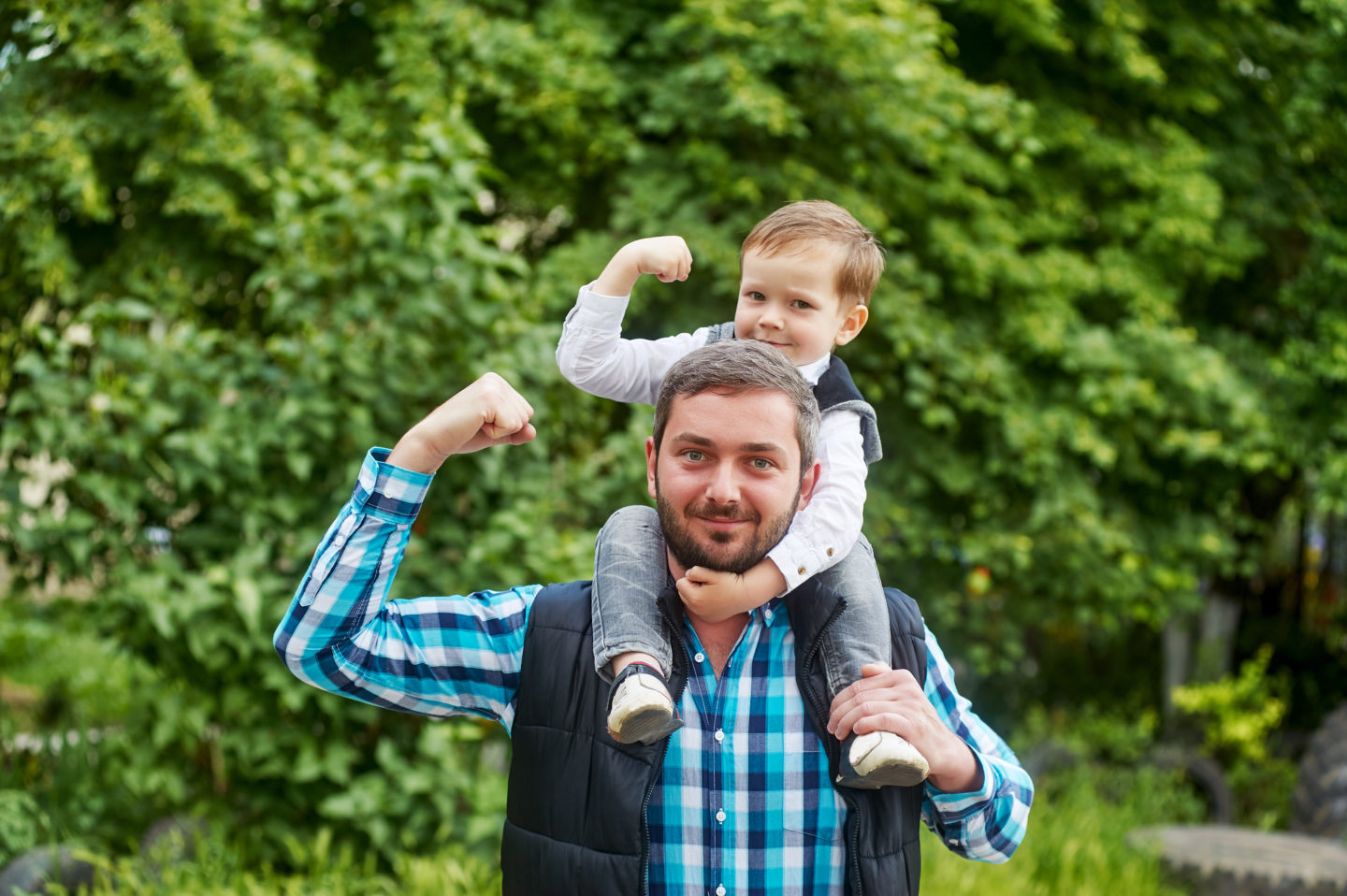 Un homme porte sur ses épaules un petite garçon de 3 ans, tous deux  montrent leur biceps.