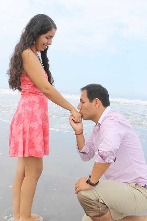 Un homme à genoux embrasse la main d'une femme sur une plage.