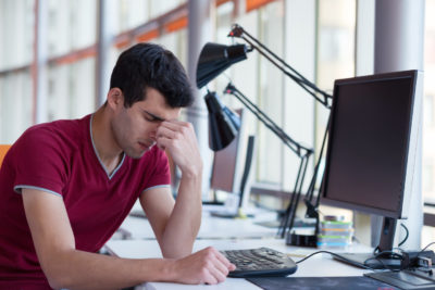 Un homme devant un ordinateur pose sa tête sur son poing d'un air découragé