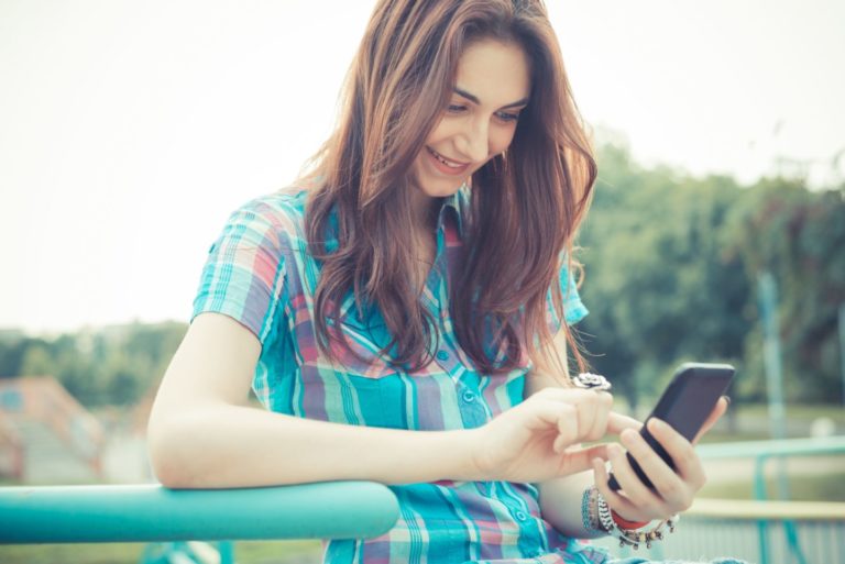 Une jeune femme tchatte sur son smartphone en souriant