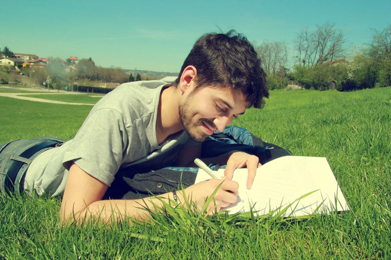 Un homme écrit sur des feuilles en souriant.