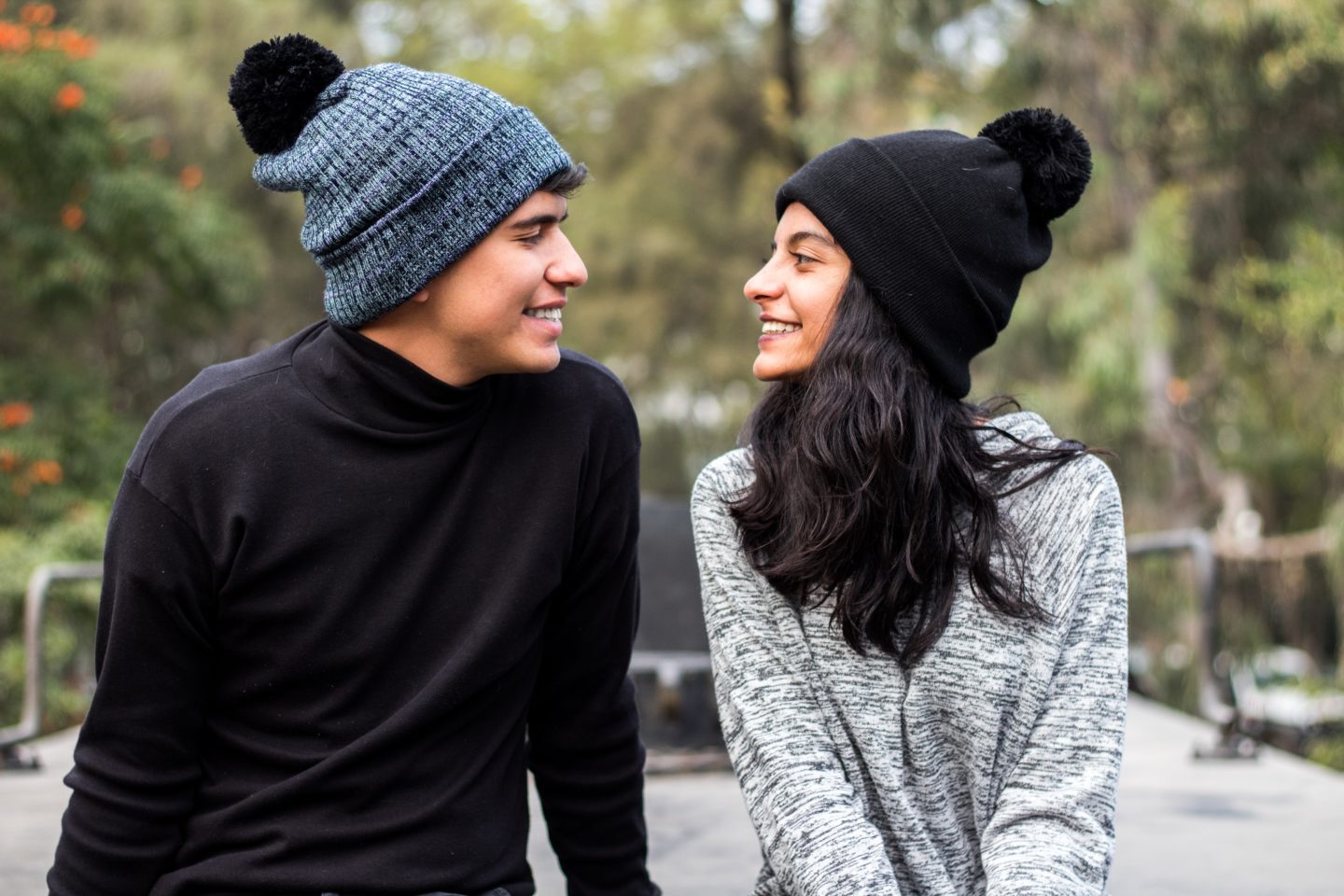 Un homme et une femme, dehors en pull avec des bonnets sur la tête, se regardent en souriant