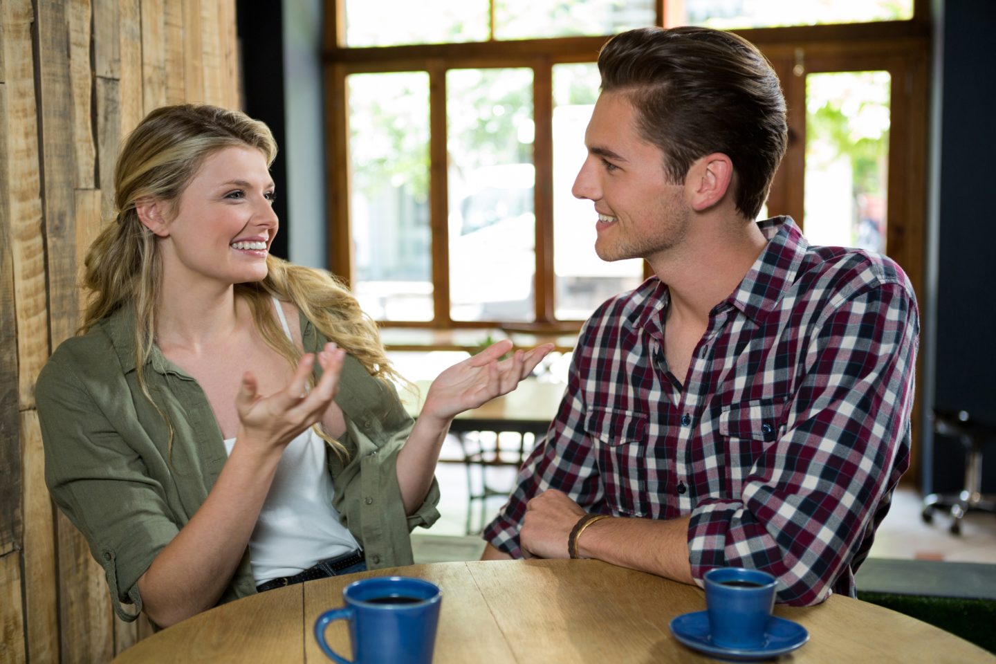 Une femme et un homme prennent un café ensemble, ils sourient et elle lève ses mains d'un air incrédule
