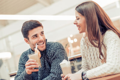 Un homme et une femme rient ensemble en buvant un café frappé. Lequel des deux va payer ?