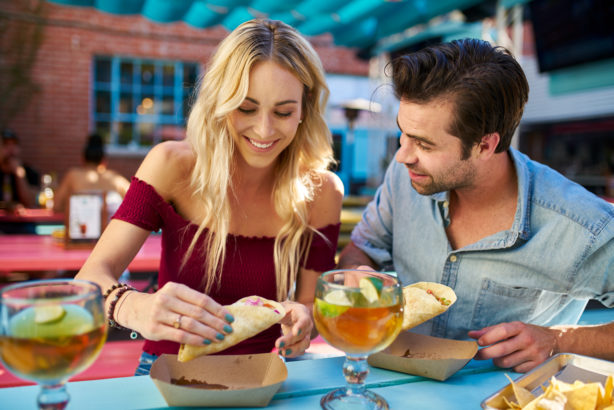 Une femme et un homme rient en se servant des tacos à un buffet. Qui va payer l'addition ?