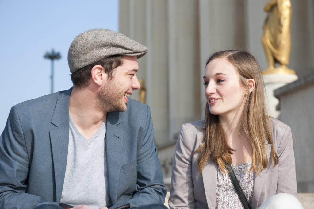Un homme et une femme discutent, assis sur des marches devant un monument