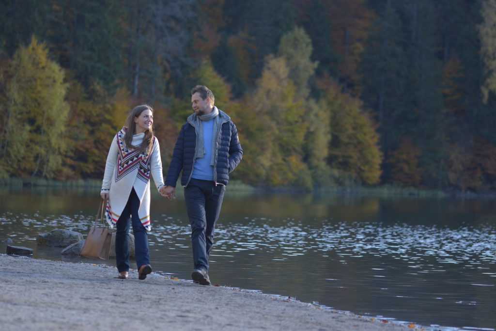 Une femme et un homme se promènent main dans la main au bord d'un lac