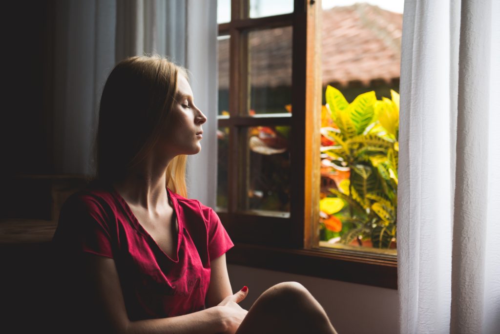 Une femme ferme les yeux à côté d'une fenêtre
