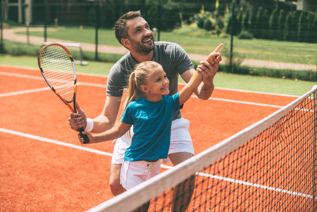 Un homme aide une petite fille à jouer au tennis